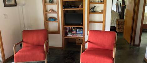 A living room with two red armchairs, a wooden bookshelf, and a flat-screen TV.