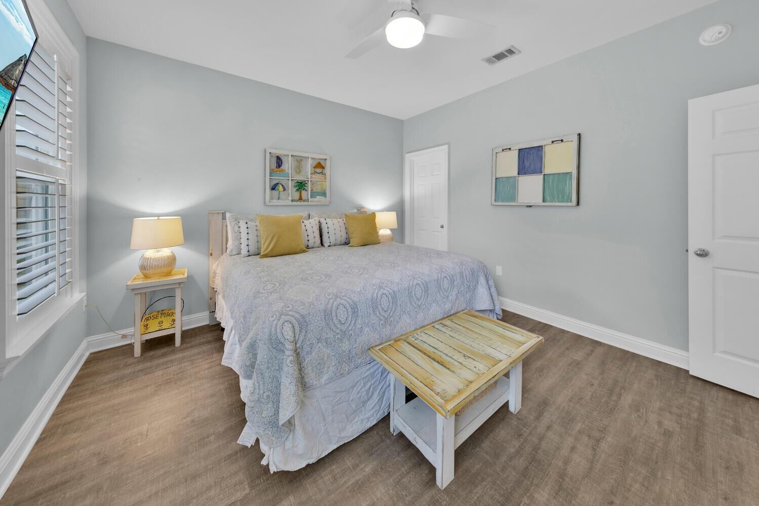 Une chambre à coucher comprenant un lit, des tables de chevet, un banc, un ventilateur de plafond et des œuvres d’art accrochées aux murs.
