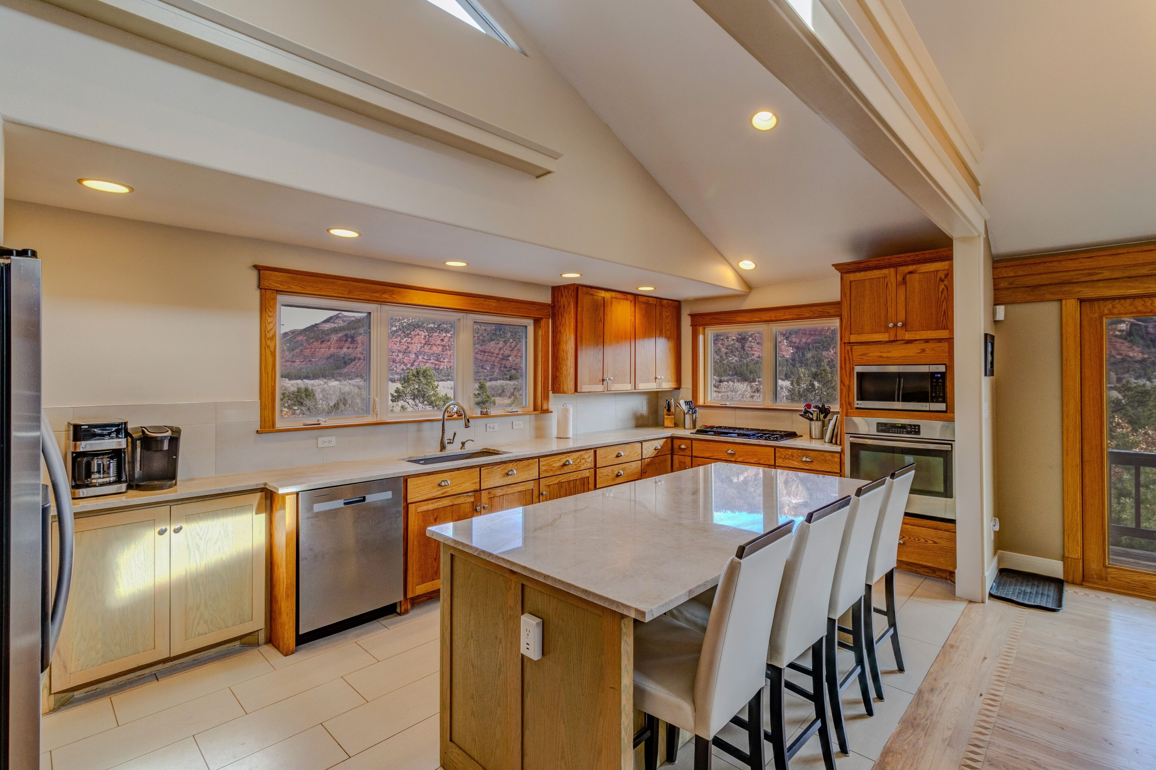 A modern kitchen with wooden cabinets, a large island, and a view of a mountainous landscape.