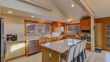 A modern kitchen with wooden cabinets, a large island, and a view of a mountainous landscape.