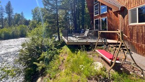 A cabin with a deck, surrounded by dense forest and a river. - Riverfront, with Hot Tub & Deck Overlooking the River! Sandy beach steps away! (Leavenworth)