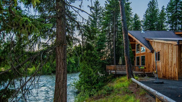 A cabin with a deck overlooking a river, surrounded by dense forest. - Riverfront, with Hot Tub & Deck Overlooking the River! Sandy beach steps away! (Leavenworth)