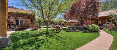 A well-maintained garden with a wooden pergola, outdoor seating, and a stone pathway.