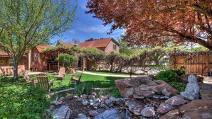 A rustic house with a red roof, surrounded by a well-maintained garden with a small pond and rocks. - The Main House (Cali Cochitta) (Moab)