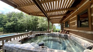 Un bain à remous installé sous une pergola en bois, avec vue sur une zone boisée.
