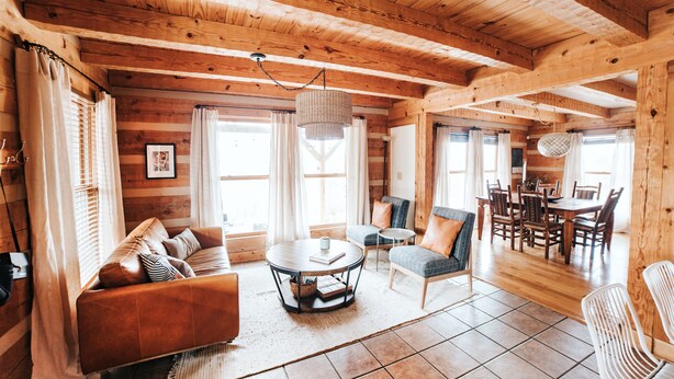 L’intérieur chaleureux d’un chalet en rondins, avec un plafond en bois, un coin repas et un salon comprenant un canapé et des fauteuils.