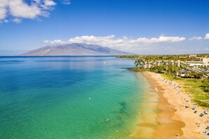 A beach with clear turquoise water, a sandy shore, and a mountain in the background. - Kihei Kai Nani - 1BR Unit, Just Steps Away From Kamaole Beach! (Kihei)