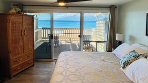 A hotel room with a bed, a wooden wardrobe, a ceiling fan, and a balcony with a view of the ocean.