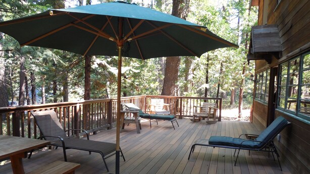 A wooden deck with outdoor furniture, including lounge chairs and a table, surrounded by trees.