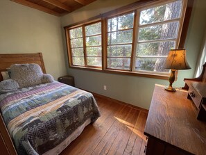 A bedroom with a wooden bed, a nightstand, a lamp, and a window with a view of trees.