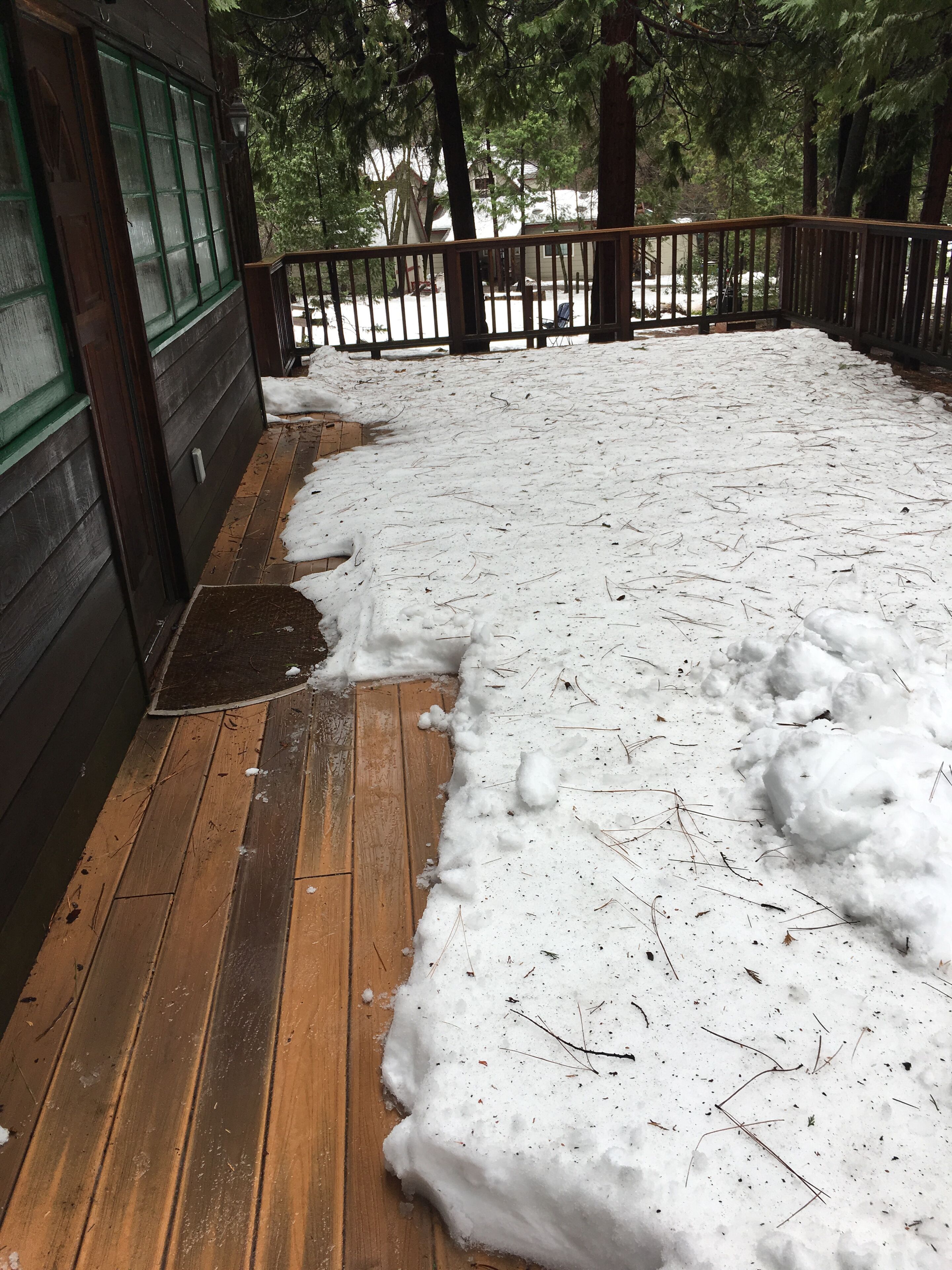 Une terrasse en bois recouverte de neige, une clôture en bois et un bâtiment dont les fenêtres sont encadrées de vert.