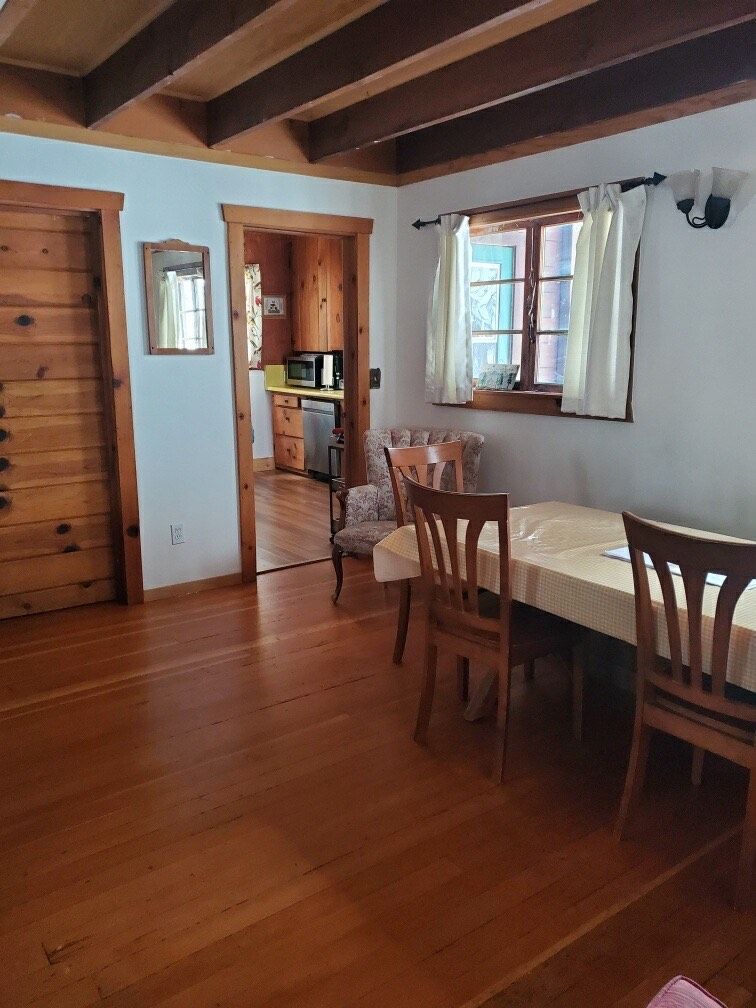 Ein Essbereich aus Holz mit Tisch und Stühlen, eine Küche im Hintergrund und eine Holztür.