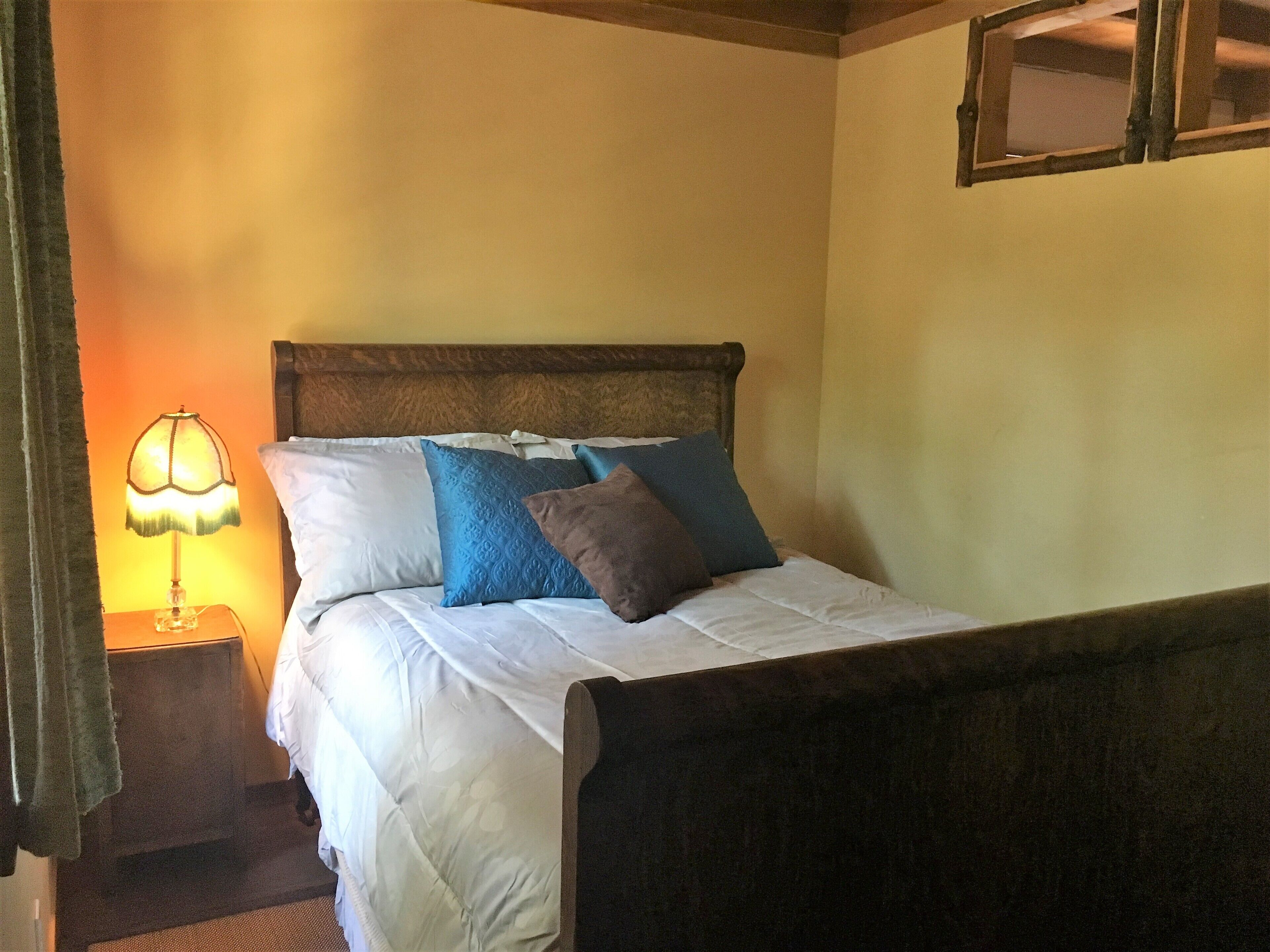 A bed with white bedding and multiple pillows, a bedside lamp, and a wooden headboard.