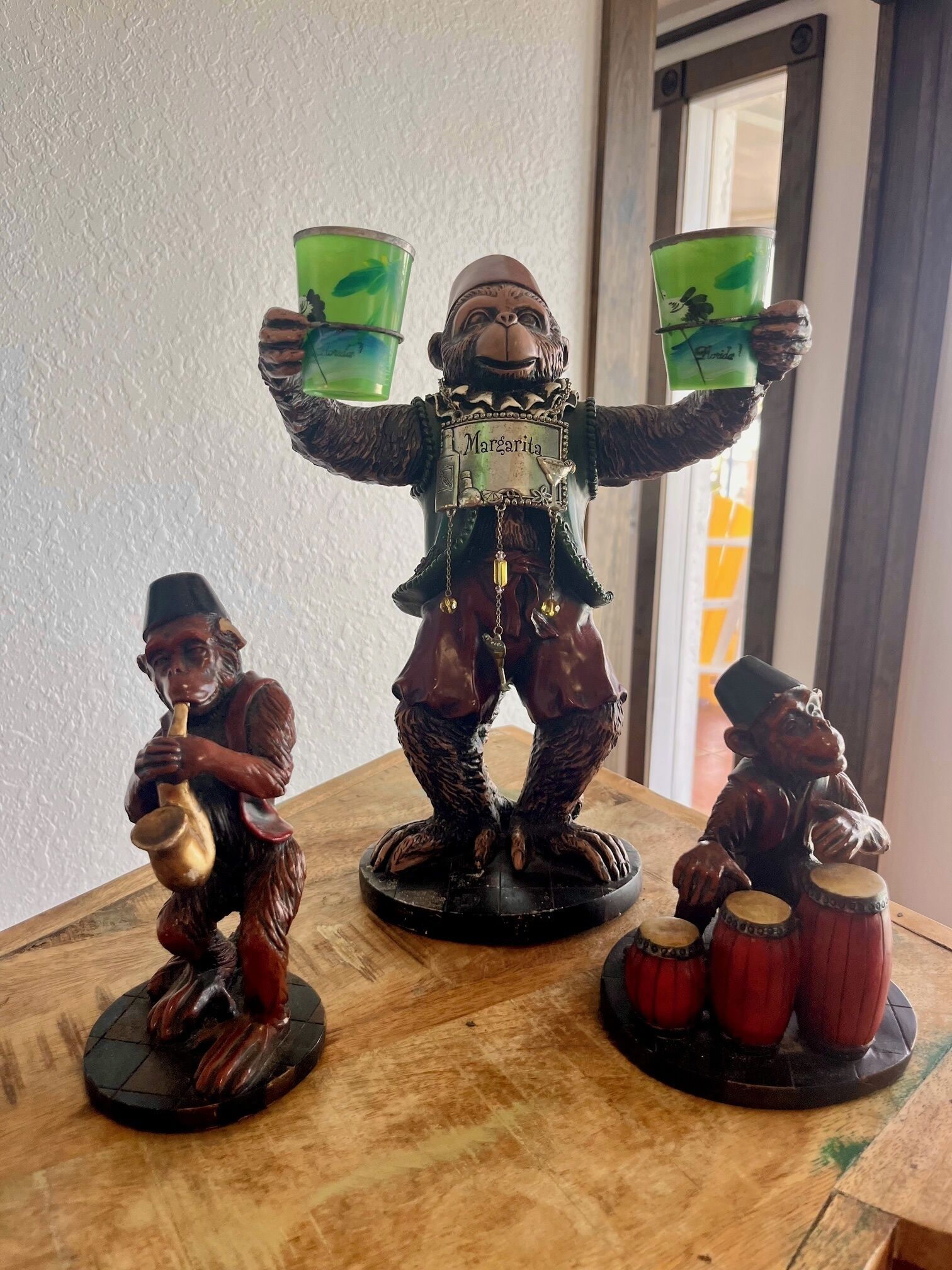 Drie aapbeeldjes op een houten tafel, elk met een ander voorwerp.