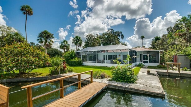 A modern house with a glass conservatory, a wooden deck, and a small pond.