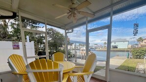 A covered patio with a table and four Adirondack chairs, overlooking a body of water and a marina.