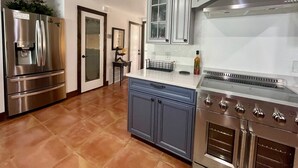 A modern kitchen with stainless steel appliances, grey cabinetry, and a tiled floor.