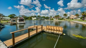 A calm waterfront with a wooden dock extending into the water, a boat docked on the left, and residential buildings in the background.