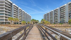 Une promenade en bois mène à un immeuble moderne doté de balcons et bordé de palmiers.