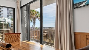 Une table en bois, agrémentée de paniers tressés, une vue sur la plage et un balcon avec des rideaux.