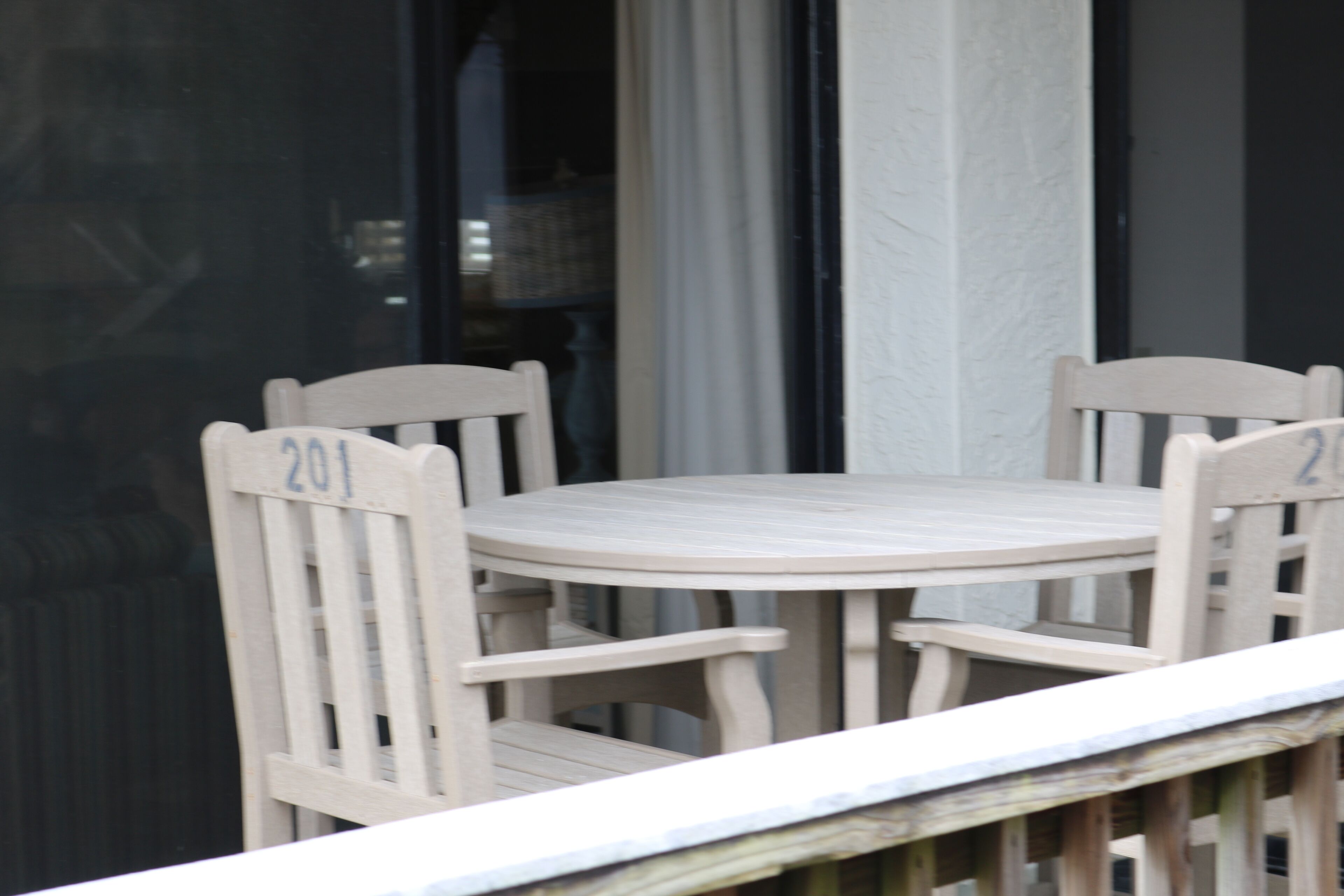 A round wooden table with four chairs, each chair marked with the number 201.