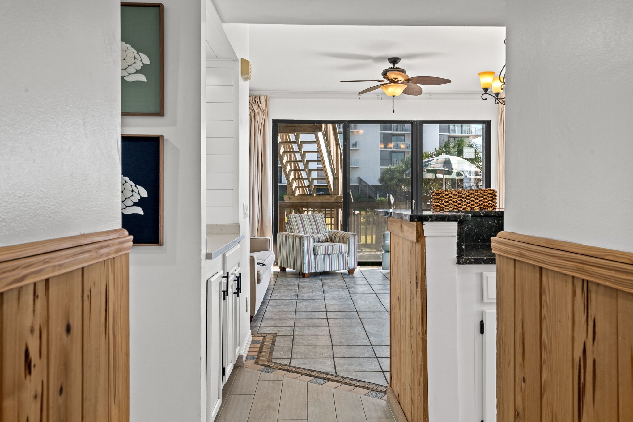 A narrow hallway with wooden paneling, a ceiling fan, and a view of a balcony with a chair and a staircase.