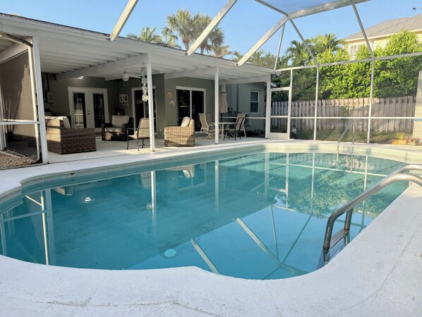 A pool area with a covered patio, outdoor furniture, and a wooden fence in the background. - Great location!!! Old Naples Pool Home - Walk to the beach, shops, restaurants. (Naples)