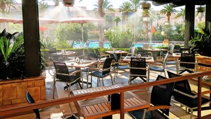 Un área de estar al aire libre con mesas y sillas, con vista a una piscina y palmeras.