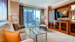 Un salón amplio con un gran ventanal, un sofá, una silla, una mesa de centro y un televisor sobre un mueble de madera.