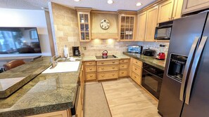 A modern kitchen with granite countertops, wooden cabinets, a stainless steel refrigerator, a built-in oven, and a microwave.