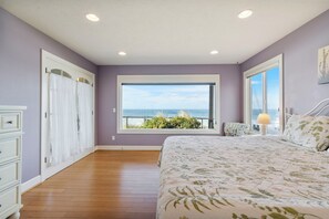 A bedroom with a large window, a bed, a dresser, and a nightstand.
