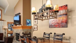 Ein Essbereich mit Holztisch und -stühlen, einem Steinkamin, einem Fernseher und Kunstwerken an den Wänden.