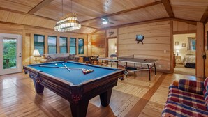 Une pièce au plancher de bois, équipée d’une table de billard, d’une table de ping-pong et d’un canapé.