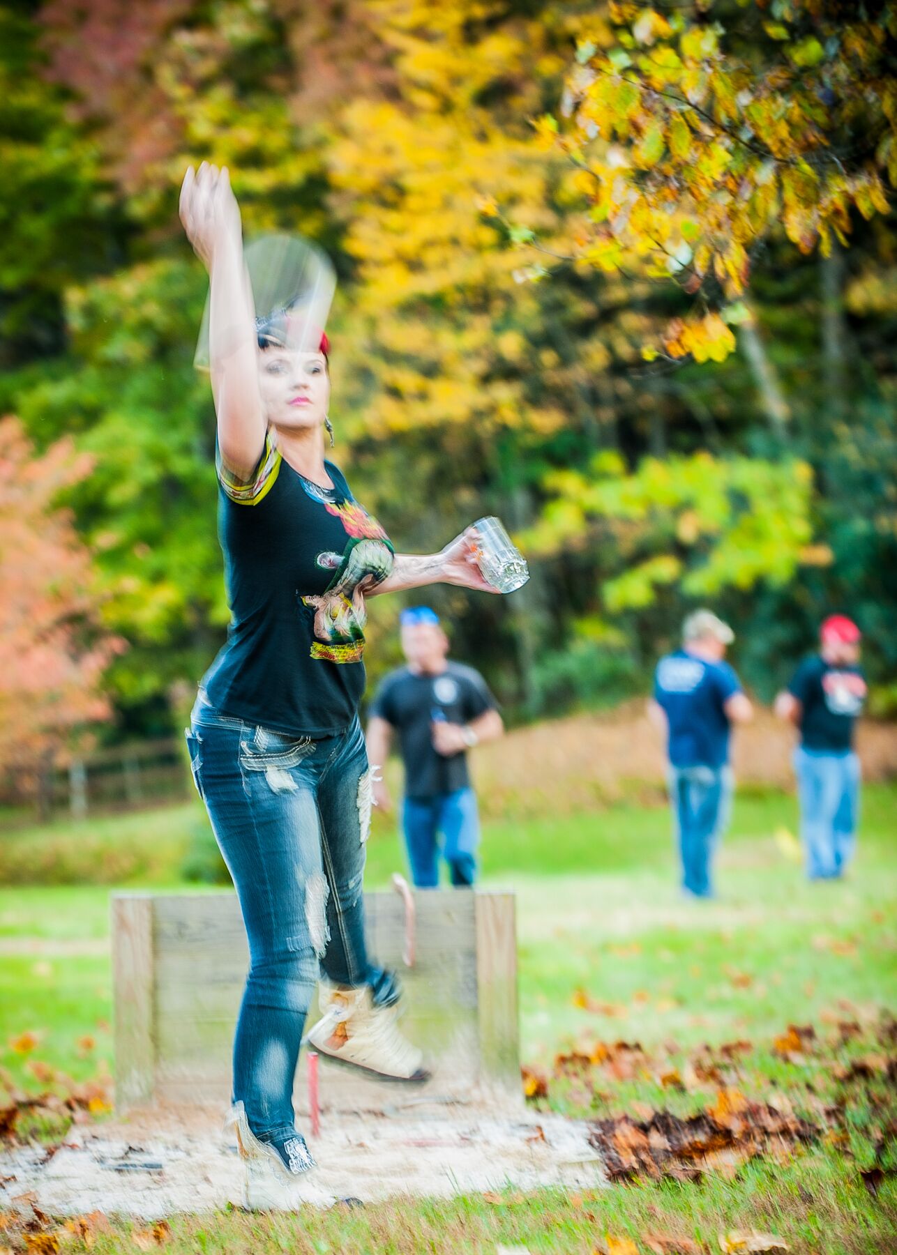 A person in a black shirt and jeans throwing a discus in an outdoor setting with trees and grass.