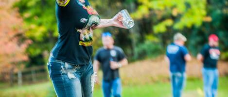 A person in a black shirt and jeans throwing a discus in an outdoor setting with trees and grass.