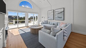 Ein geräumiges Wohnzimmer mit großem Fenster, einem grauen Sofa und einem Holztisch.