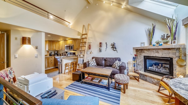 A spacious living area with a fireplace, wooden furniture, and a kitchen in the background.