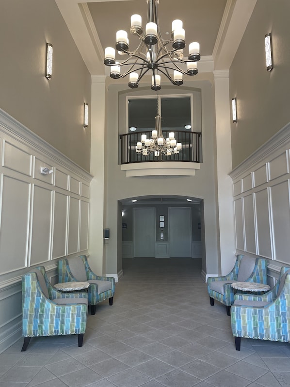 A spacious lobby with a high ceiling, a central chandelier, and two seating areas with patterned chairs.