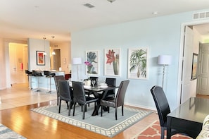 A dining area with a rectangular table, six chairs, and a rug. There are framed botanical prints on the wall.