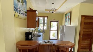 A compact kitchen with a sink, stove, and refrigerator. There are two wooden stools at the counter. -  Bayblue Suite1  (Caye Caulker)