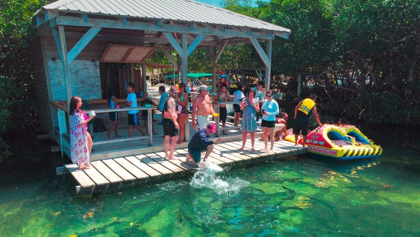 A wooden dock extending into clear water with people standing on it. -  Bayblue Suite1  (Caye Caulker)