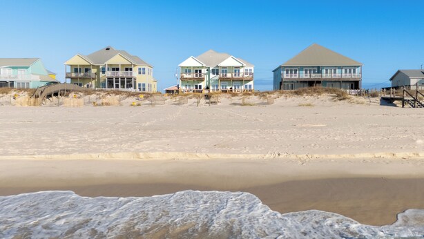 A beachfront property with multiple houses, a sandy beach, and waves approaching the shore.