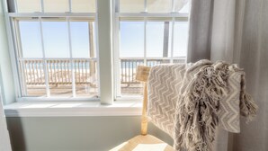 A room with a view of the beach through a window, a wooden chair, and a textured throw blanket.