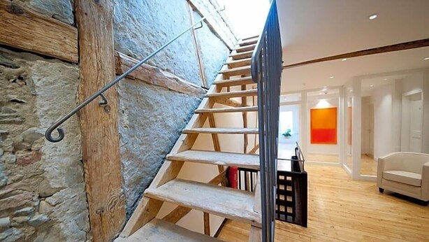 A wooden staircase with a metal handrail, leading to a room with a white chair and a bright orange accent wall. - Hotel Engel Lindauer Bier Und Weinstube (Lindau)