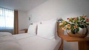 A hotel room with a bed, a nightstand, a lamp, and a vase of flowers. - Hotel Engel Lindauer Bier Und Weinstube (Lindau)