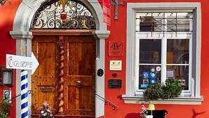 A red building with a wooden door, a sign for Hotel Engel, outdoor seating with tables and chairs, and a rope barrier. - Hotel Engel Lindauer Bier Und Weinstube (Lindau)