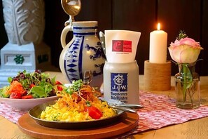 A dining table with a plate of food, a coffee cup, a candle, and a vase with a flower.