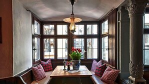 A bay window seating area with a table, bench, and decorative vase with flowers. - Hotel Engel Lindauer Bier Und Weinstube (Lindau)