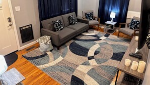 A living room with a grey sofa, two armchairs, a patterned rug, and a small table with a lamp and remote control. - 2BR 1BATH Cozy Cottage Quiet Area! 12mins-Downtown Nashville 10mins-Brentwood! (Nashville)