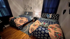 A bedroom with two beds, each with patterned bedding and pillows, a small bedside table with a lamp, and a wall-mounted heart decoration. - 2BR 1BATH Cozy Cottage Quiet Area! 12mins-Downtown Nashville 10mins-Brentwood! (Nashville)